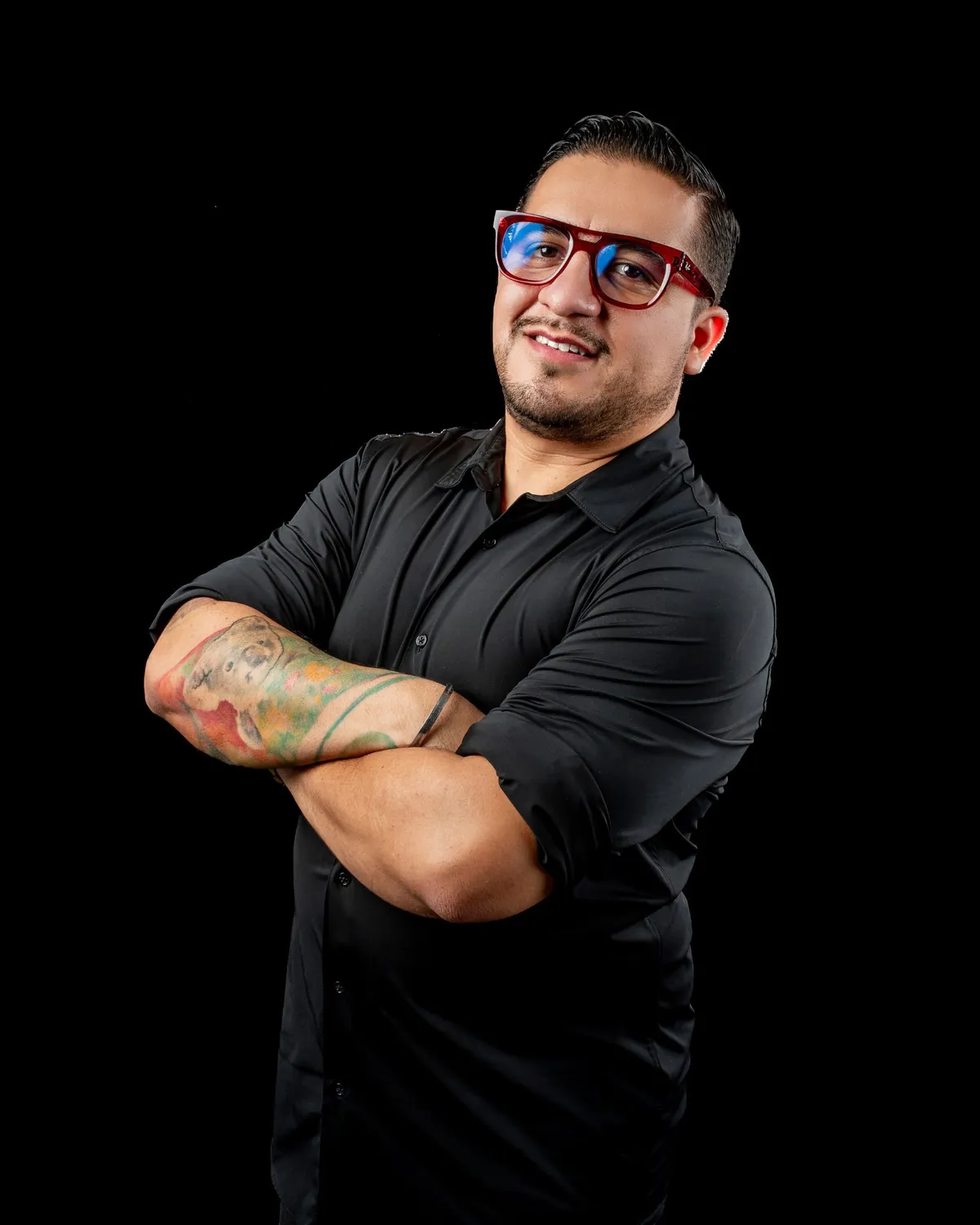 Rik Landeros con lentes rojos y los brazos cruzados, sonriendo a cámara